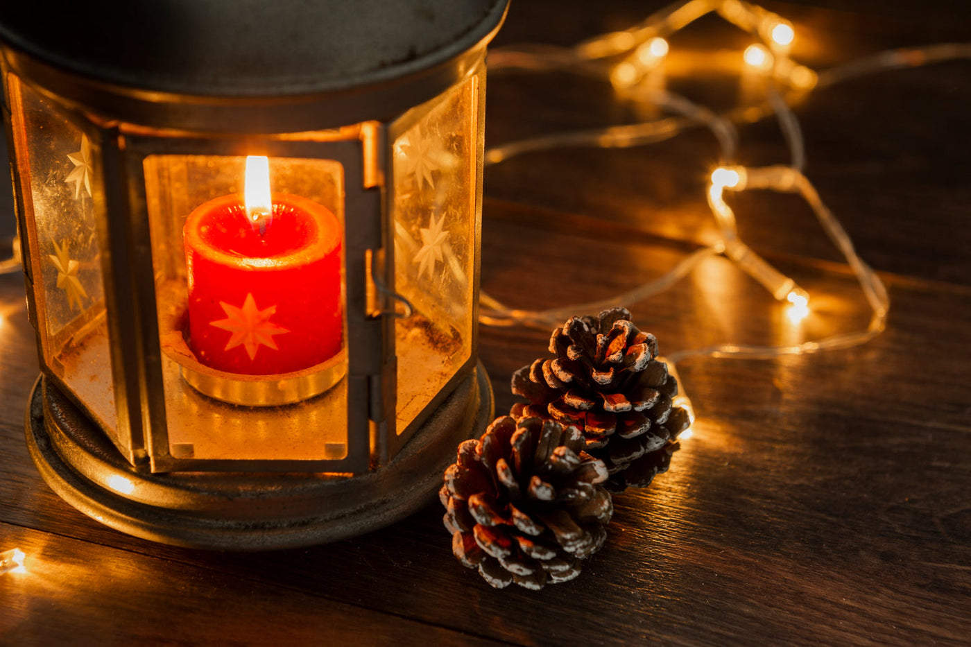 A red candle inside a Christmas lantern, styled with pinecones and lights for a festive tabletop display.