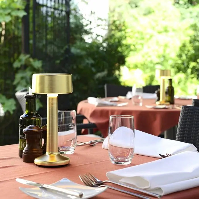 Imagilights Moments cylinder Gold table lamp placed on an outdoor dining table setting.