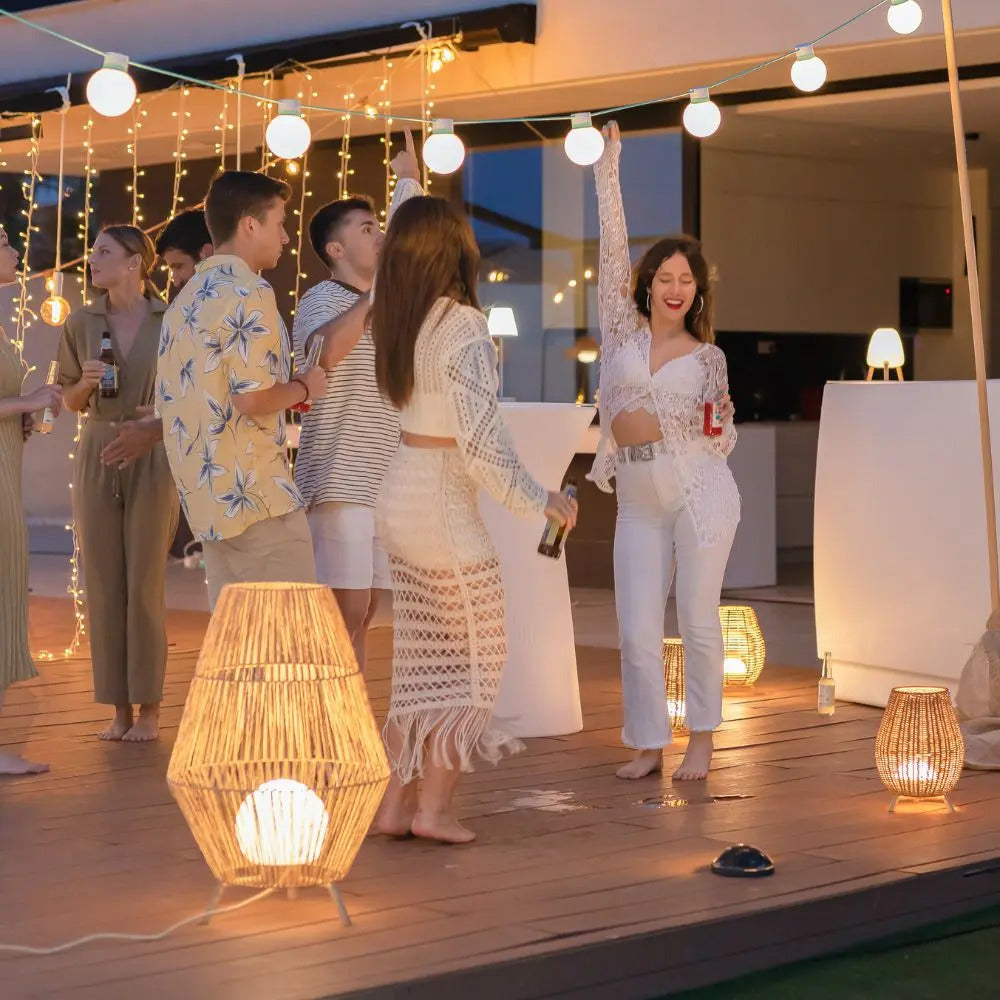 Group of people enjoying an outdoor evening gathering with outdoor home lights, including exterior string lights and floor lamps creating a warm atmosphere.
