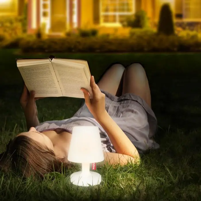Woman reading a book on the grass at night with a portable study lamp glowing beside her.