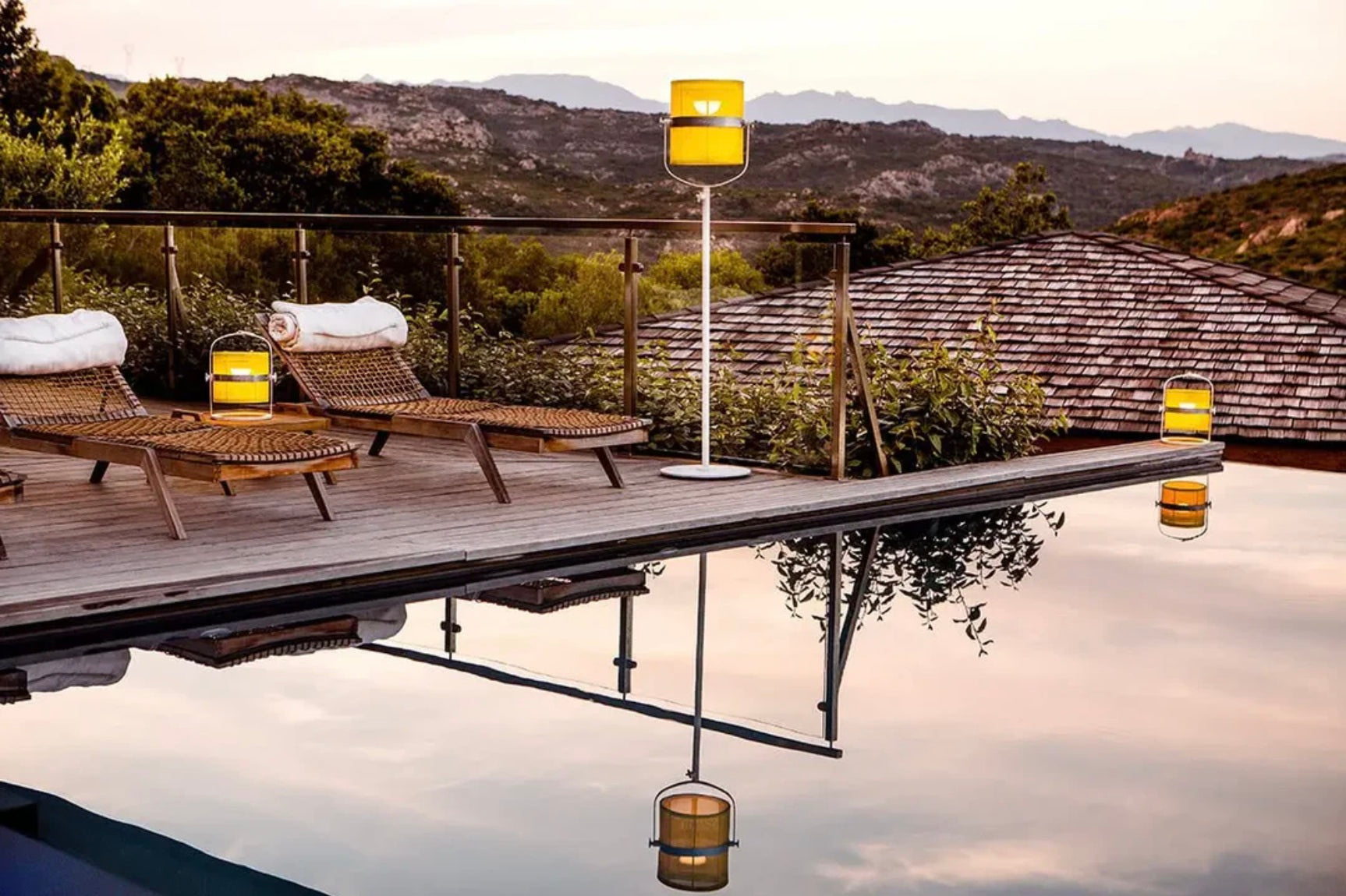 Maiori La Lampe Paris and La Lampe Petite solar outdoor floor lamps on a wooden poolside deck, creating soft ambient lighting at sunset in a luxury resort setting